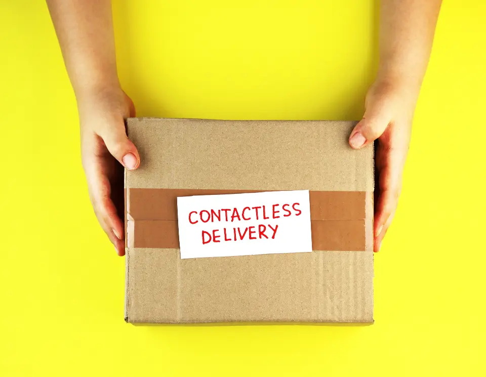 hands holding parcel showing contactless deliver on the box, yellow background
